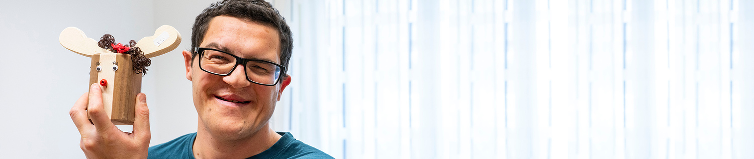 Ein Mann zeigt sein selbstgemachtes Rentier aus Holz in die Kamer