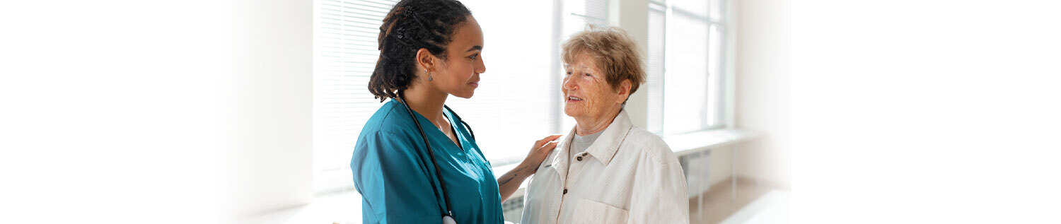 Das Foto zeigt eine ältere Patientin und eine Pflegerin, die ihre Hand auf die Schulter der Patientin legt.