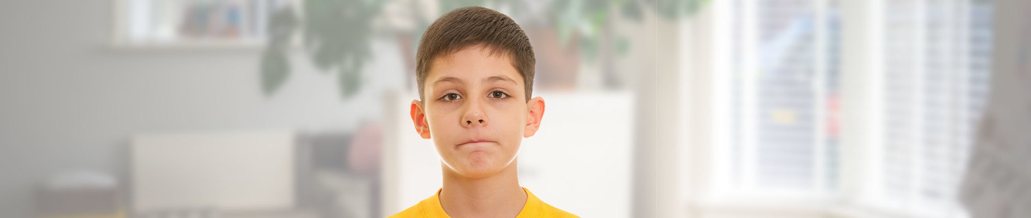 Das Foto zeigt einen Jungen der mit verkniffenen Lippen direkt in die Kamera blickt.