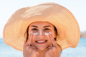 Die Frau trägt sich gerade Sonnencreme im Gesicht auf. 
