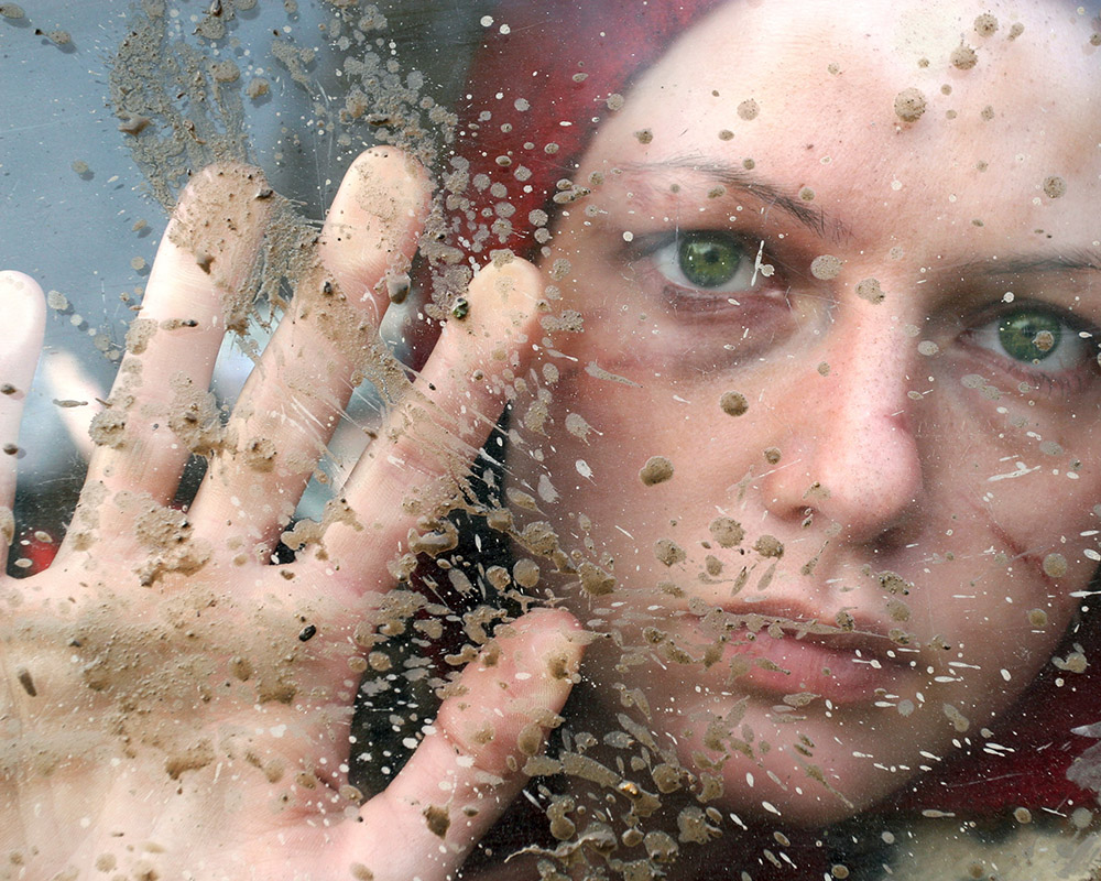 Gewaltbetroffene Person hinter Glasscheibe