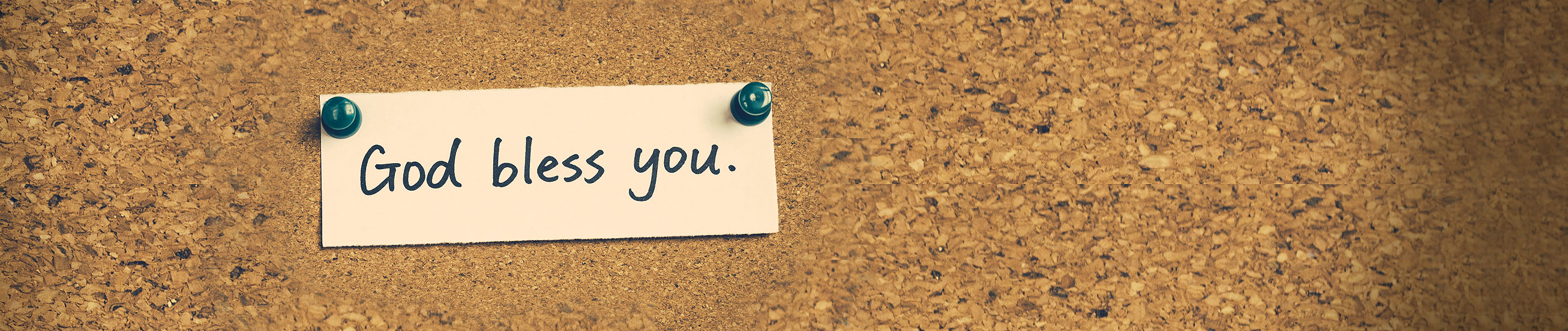 Das Bild zeigt eine Pinnwand mit Zettel und dem Wortlaut 'God bless you'