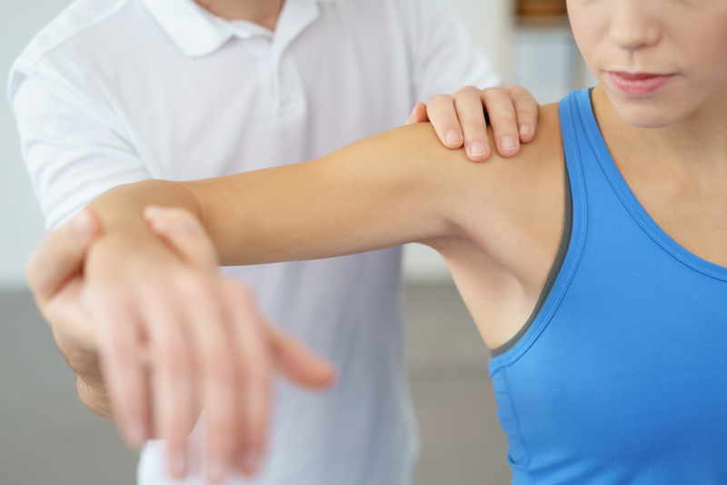 Close up Professional Physical Therapist Lifting the Arm his Female Patient While Examining the Injured Shoulder.