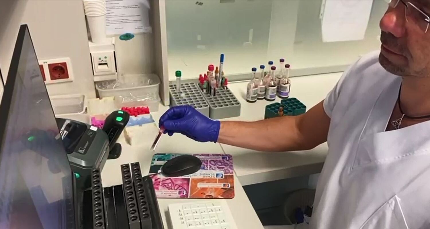 Zu sehen ist ein Mitarbeiter vor einem PC mit Probenröhrchen.