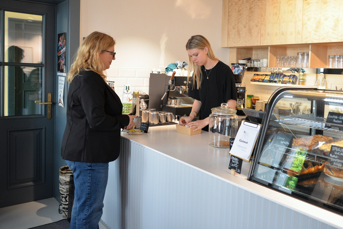 Das Bild zeigt eine Mitarbeiterin, die hinter der Theke etwas für eine Kundin verpackt.