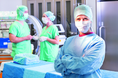 Im Vordergrund ist eine Gefäßchirurgin zu sehen und im Hintergrund ein Kollege und eine Kollegin im OP