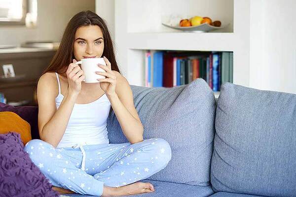 Das Bild zeigt eine junge Frau, die eine Tasse Tee in der hält und auf einer Couch sitzt.