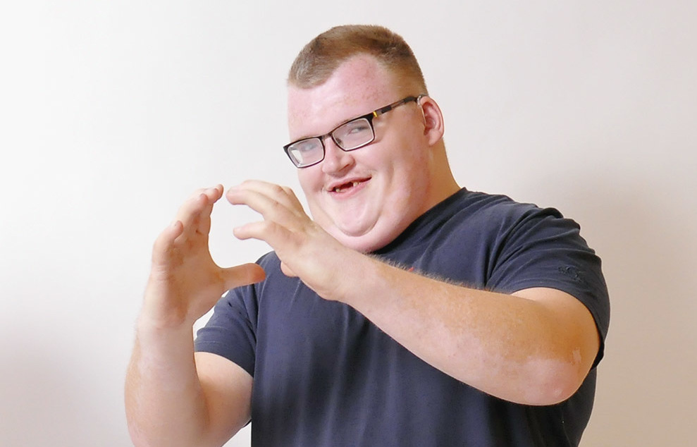 Ein junger Mann zeigt eine Gebärde und lächelt