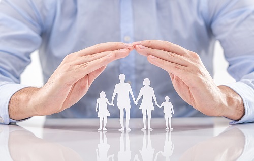 Zwei Hände die aus Papier gebastelte Familie umhüllen