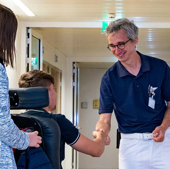 Das Foto zeigt einen Arzt, der einem Patienten im Rollstuhl die Hand schüttelt.