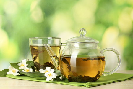 green tea with jasmine in cup and teapot on wooden table on green background
