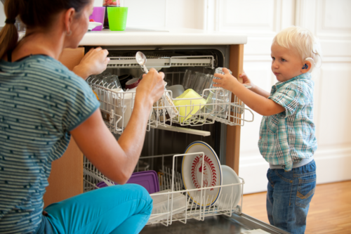 Das Foto zeigt eine Frau und ein kleines blondes Kind, das gerade den Geschirrspüler ausräumt.