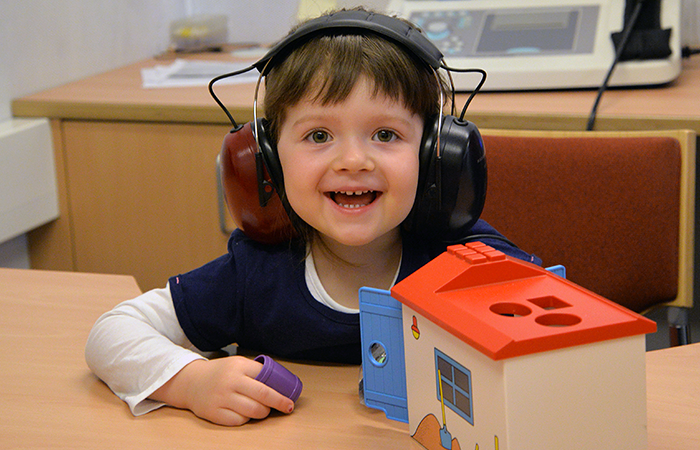 Das Foto zeigt ein Mädchen bei einer Untersuchung in der EMA. Es hat Kopfhörer auf und vor ihr steht ein Spielzeughaus.