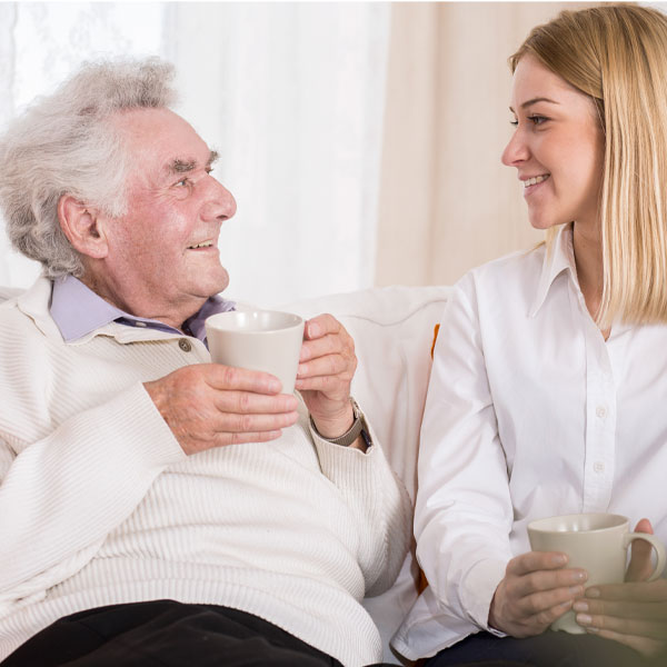 Das Foto zeigt einen Bewohner mit einer Tasse in der Hand und eine Pflegerin 