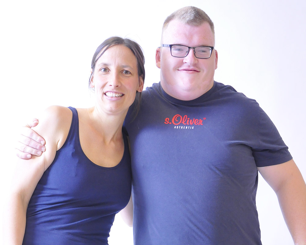 Ein Kunde legt den Arm um eine Mitarbeiterin. Beide lächeln. 