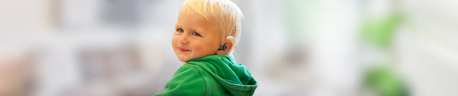 Das Foto zeigt einen kleinen blonden Jungen mit einem Cochlea-Implantat