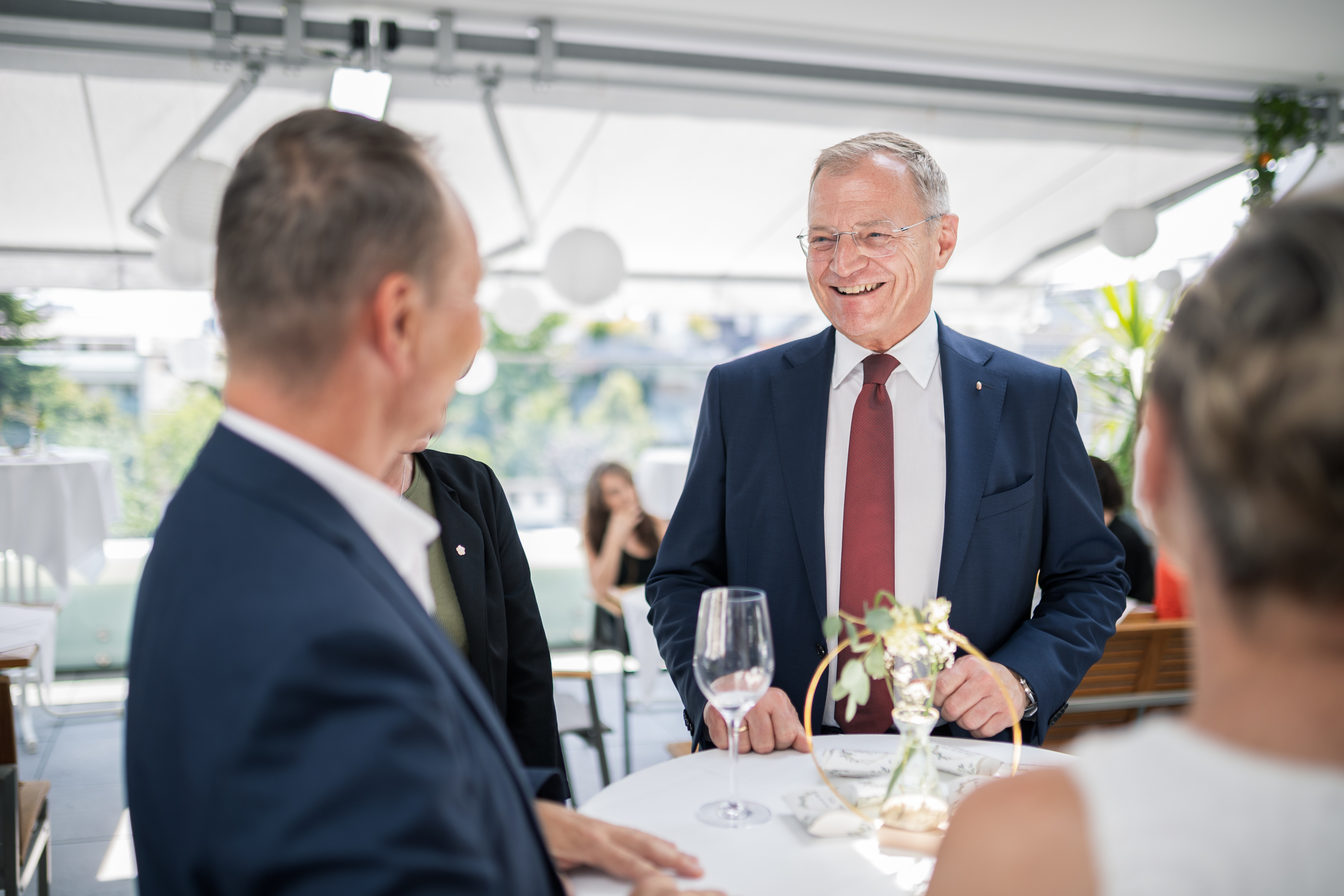 Der Landeshauptmann lacht an einem runden Stehtisch gemeinsam mit den anwesenden Personen.
